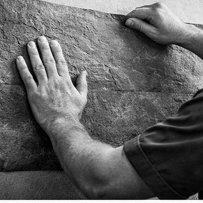 Two hands press a Flexistone sheet flat against a wall and align its top edge, black and white